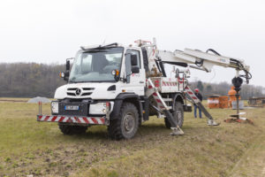 Image d'un UNIMOG U530 carrossé avec une grue RISA 74TA30, capacité de levage 7400kg à 3 mètres de l'axe de la grue. Stabilisateurs panthographiques, moteur de forage POCLAIN MS35, tarière désagrégatrice, radio-commande télécommande pour la commande du fonctionnement de la grue.